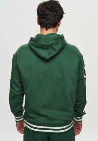 Hoodie vert en matériau doux, doté d'une poche kangourou, d'une capuche et de poignets et d'un ourlet rayés. Accent du logo sur la manche.