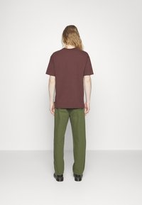 Vínová tričko s krátkými rukávy, volný střih a kulatým výstřihem. Spárováno se zelenými kalhotami, viditelnými švy a černou obuví.