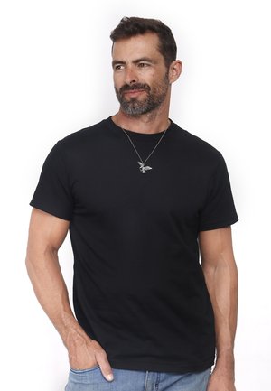 Zwarte crewneck t-shirt van katoenstof, korte mouwen, ontspannen pasvorm, gecombineerd met denim jeans en een zilveren hangertje.