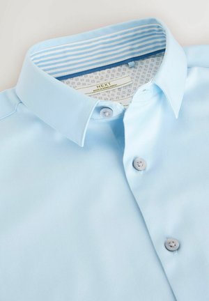 Svetlo modra kratka srajca s ostrim ovratnikom, ki ima diskretne gumbne podrobnosti in črtasto notranjo oblogo ovratnika.