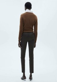 Un pull en maille marron avec un col blanc, associé à un pantalon ajusté vert foncé. Le modèle est vu de dos, mettant en valeur la silhouette de la tenue.