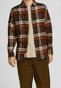 Camicia di flanella a quadri marrone e arancione con design a bottoni, colletto, maniche lunghe e texture morbida sopra una maglietta beige.