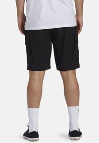 Sort cargo shorts med sidelommer, lavet af letvægtsmateriale, der fremviser en afslappet pasform. Kombineret med hvide sokker og sorte sneakers.