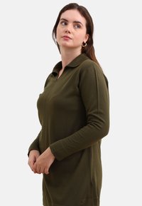 Olijfgroen langslijfs polo-jurk met een kraag, ribbelstructuur en een rechte snit. Heeft een voorkant met knoopsluiting en manchetten.