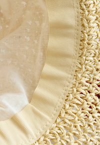 Napperon rond avec une base en paille tissée, orné d'un bord en tissu texturé jaune et d'un superposé transparent à motifs.