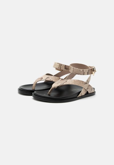 Sandales plates noires avec des brides beige imprimé serpent, dotées de boucles pour les orteils et d’une fermeture à boucle à la cheville.