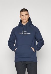 Sweat à capuche bleu marine avec une poche kangourou, un cordon de serrage et un texte blanc indiquant « Peak Performance » sur la poitrine. Tissu doux et texturé.