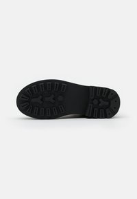 Suela de zapato de goma negra con un patrón texturizado, que presenta múltiples crestas y un detalle hexagonal en el centro para tracción.