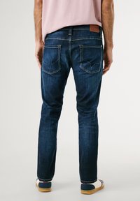 Mörkblå jeans i denim med rak skärning, med bakfickor med spetsiga flappar och kontrasterande sömmar. Bärs med avslappnat fotarbete.