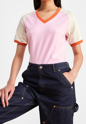 Lyserød kortærmet V-hals t-shirt med orange detaljer og cremefarvede ærmer, parret med mørk denimbukser med gyldne spænder og lommer.