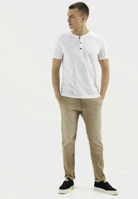 Witte korte mouwen henley-shirt met drie zwarte knopen, gecombineerd met lichtbeige tapers en zwarte sneakers. Glad materiaal, casual pasvorm.