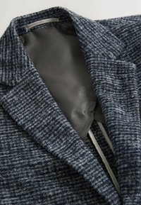 Sacou din material texturat de culoare albastru-gri, cu un rever tip notch și căptușeală netedă. Prezintă o croială adaptată și umeri structurați.
