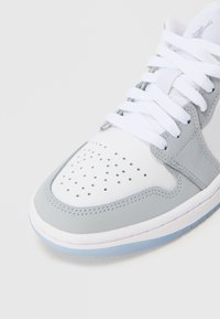 Szaro-biały sneaker wykonany ze skóry i zamszu, z perforowanym przodem buta, wyściełanym kołnierzem i płaskimi sznurowadłami. Uzupełniony przezroczystą podeszwą.