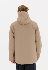 Beige vattentät jacka med huva, med rak passform, långa ärmar och sömmar på baksidan. Inga synliga logotyper eller mönster.