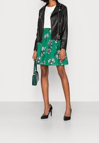 Zwarte leren motorjack, witte top, groene bloemenrok, zwarte hoge hakken en een gestructureerde groene handtas. Heeft bloemmotieven.