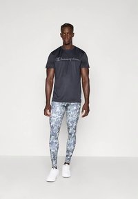 Maglietta sportiva nera con logo "Champion", abbinata a leggings mimetici blu-grigi. Modello indossa scarpe da ginnastica bianche. Design semplice e aderente.