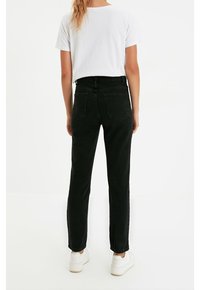 Vaqueros de denim negro con corte recto, cintura alta y cinco bolsillos, combinados con una camiseta blanca sencilla y zapatillas blancas.