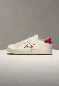 Λευκό sneaker χαμηλού προφίλ με κόκκινη πίσω λωρίδα και κόκκινο κείμενο με πλάγια γραφή ""From me to you"" στη πλευρά, τοποθετημένο σε ουδέτερη επιφάνεια.