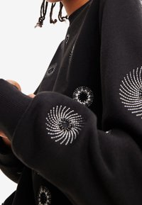 Czarna bluza z okrągłym dekoltem, ozdobiona spiralnymi srebrnymi haftami, z dzianinowymi mankietami i miękką teksturą, o lekko luźnym kroju.