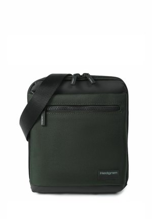 Sac bandoulière compact vert foncé avec poche zippée à l'avant, bandoulière noire réglable et logo Hedgren dans le coin inférieur avant.