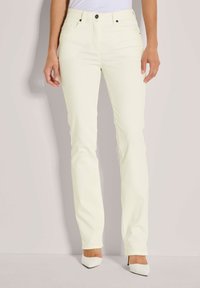 Lichtgele, recht gesneden spijkerbroek met steekzakken aan de voorkant, zichtbare stiksels en een knoopsluiting. Gecombineerd met puntige witte hakken.