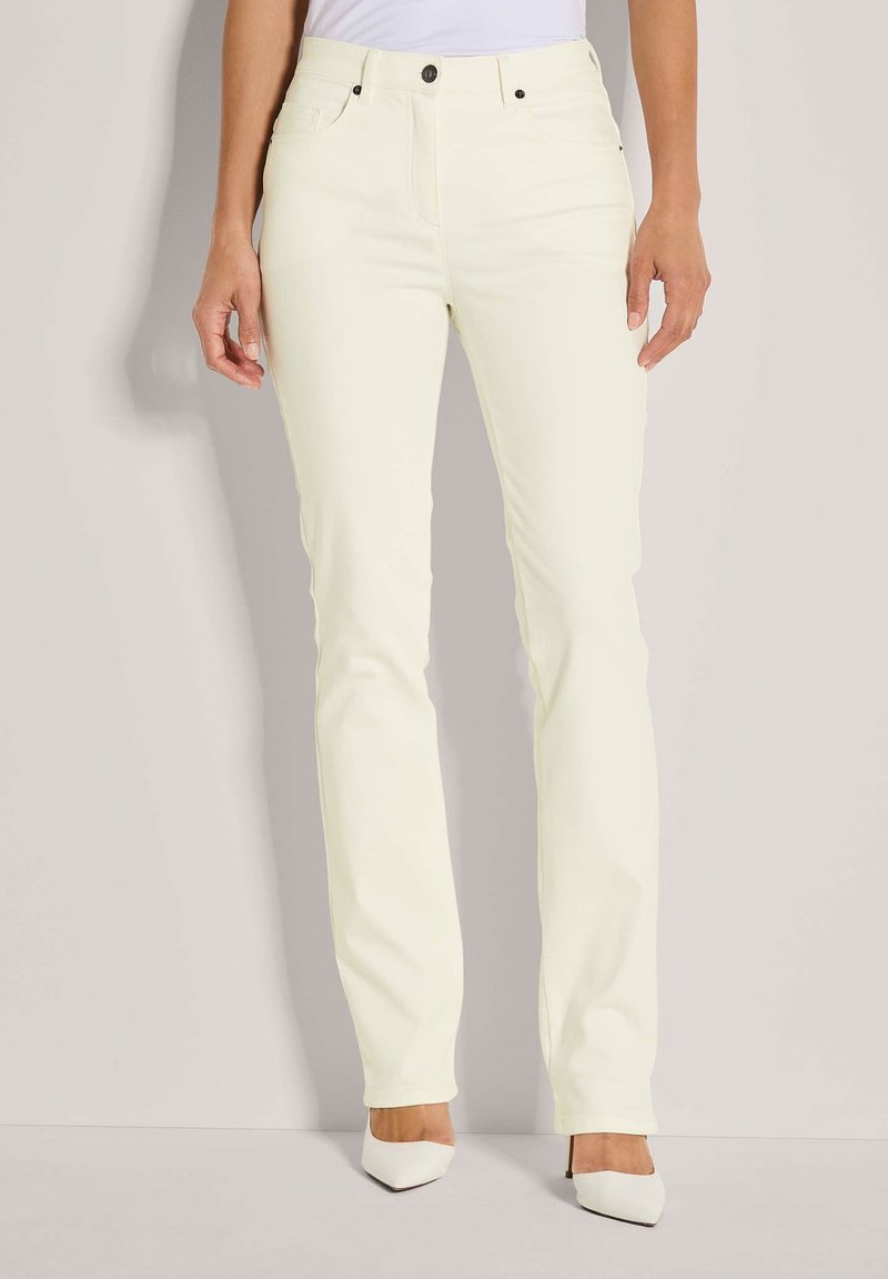 Lichtgele, recht gesneden spijkerbroek met steekzakken aan de voorkant, zichtbare stiksels en een knoopsluiting. Gecombineerd met puntige witte hakken.