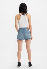 Ljusblå denimshorts med fransad nederkant, två bakfickor och en brun läderpatch i midjan. Matchat med en vit linne och svarta stövlar.