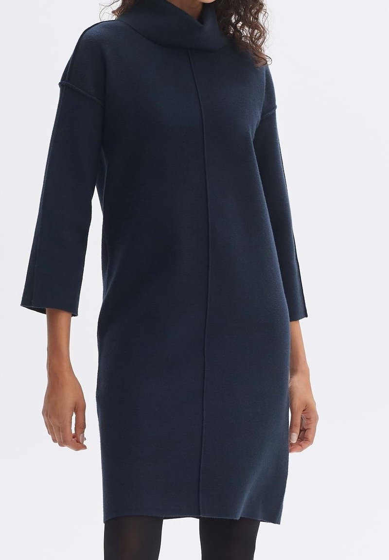 Robe en maille bleu marine avec un col bénitier et des manches trois-quarts, présentant une coupe droite et des coutures minimales. Texture lisse.