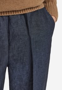 Mörkblå linnebyxor med en strukturerad yta, utrustade med veck fram och sidfickor, kombinerade med en brun stickad tröja.