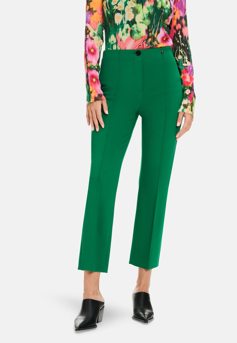 Grüne schmal geschnittene Hosen mit geradem Schnitt, hoher Taille, Seitentaschen und glatter Textur, kombiniert mit einem bunten, floral gemusterten Langarmoberteil.