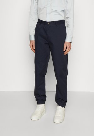 Námořnické modré kalhoty s volným střihem, vyrobené z bavlny, s knoflíkovým zapínáním a bočními kapsami, doplněné bílými teniskami.