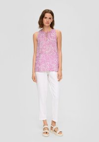 Top rosa senza maniche con pattern floreale e dettaglio al collo a fiocco, abbinato a pantaloni bianchi a sigaretta e sandali beige chiaro.