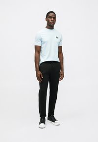 Gaiši zils īsām piedurknēm T-krekls ar mazu melnu logotipu, kombinēts ar melnām sporta biksēm un melniem teksturētiem apaviem ar baltām zolēm.