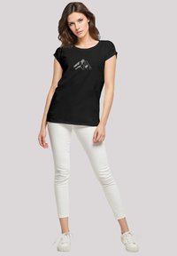 Zwarte T-shirt met korte mouwen met een witte bergafbeelding, gecombineerd met witte skinny jeans en witte sneakers.