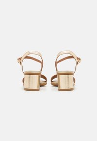 Gold heeled sandals with a block heel, tan straps, and an ankle buckle. Smooth material with an open-toe design and minimalistic construction.