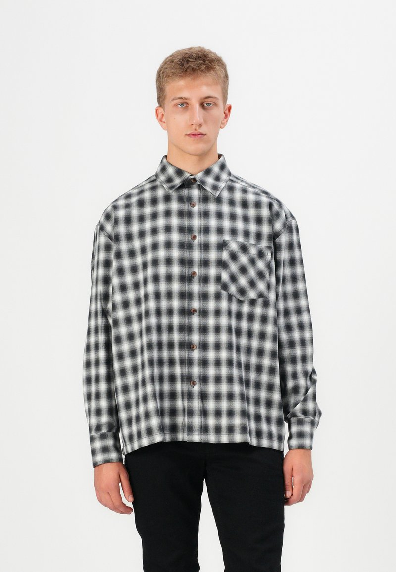 Button-up shirt in black and white check pattern, made of fabric with a soft texture. Features a chest pocket and brown buttons.