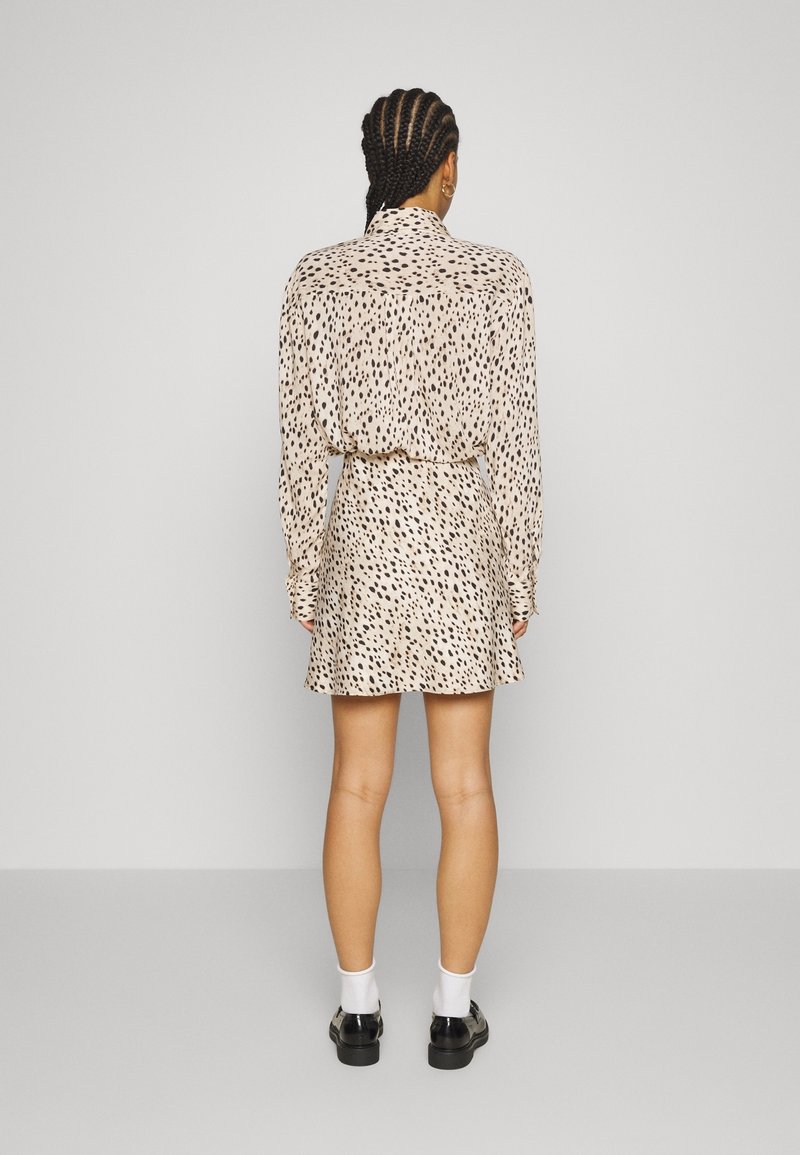 Kratší rukávový béžový šaty s černým puntíkovaným vzorem, s páskem v pase a úplným sukní. Nosené s černými botami a bílými ponožkami.