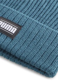 Teal knitted beanie with ribbed texture, featuring a black rectangular label with "PUMA" in white text. Soft, warm material.