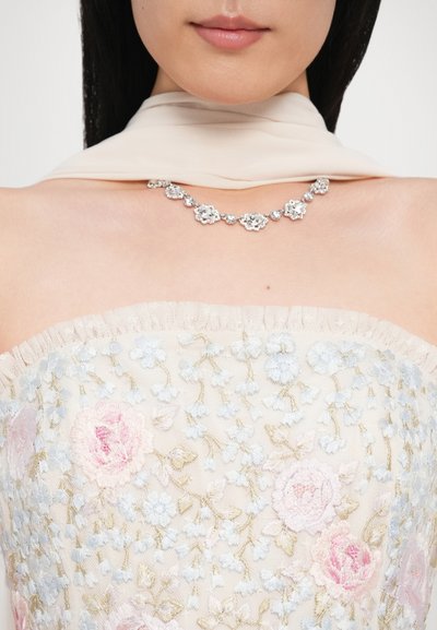 Top bez ramiączek ozdobiony koralikami i kwiatową haftem w odcieniach różu i niebieskiego, dopełniony srebrnym naszyjnikiem z kwiatowymi akcentami.