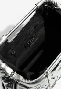 Hõbedasest metallist käekott, millel on puhvdesain, hõbedane kett aksessuaarina ning must sisu, mis sisaldab tõmblukkude taskut ja brändi silti.