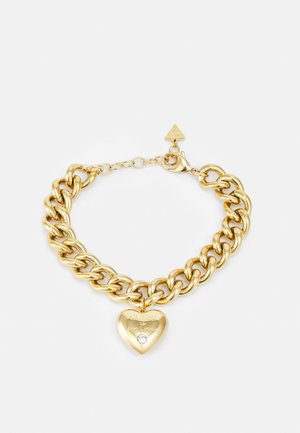Armband met goudkleurige ketting en een hartvormige hanger met de gravure "GUESS for Lovers" en een kleine, heldere edelsteen onder de tekst.