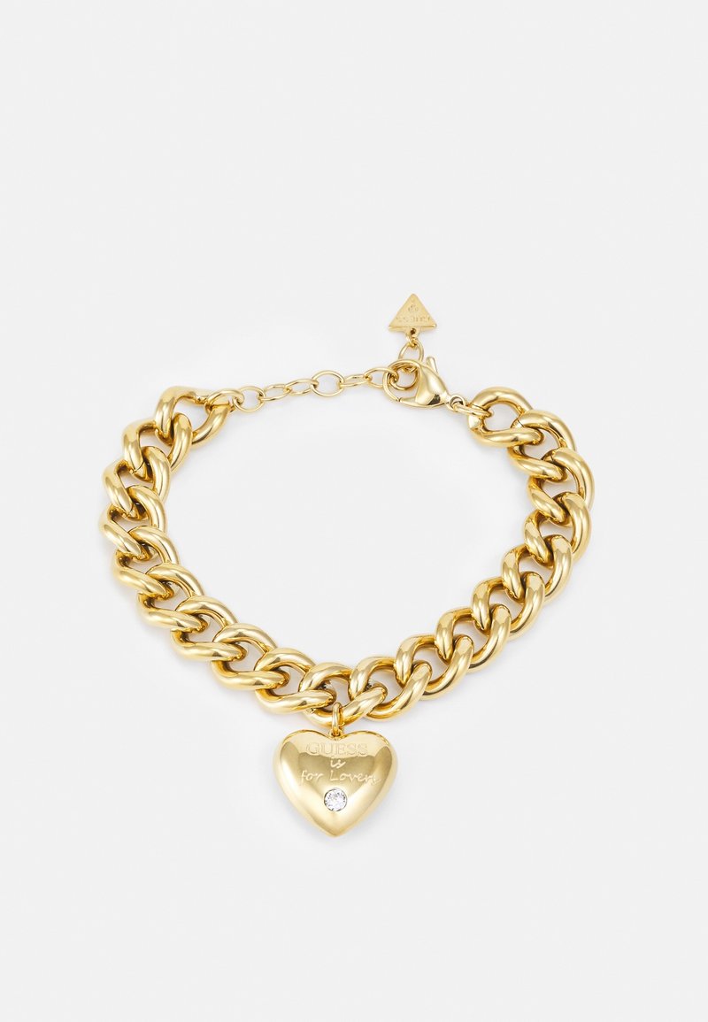 Bransoletka na łańcuszku w złotym odcieniu z zawieszką w kształcie serca z grawerem "GUESS for Lovers" oraz małym przezroczystym kamieniem pod napisem.