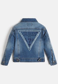 Sininen farkkutakki, jossa on kolmiomallinen logopatsas, jossa on rispaantuneet reunat. Klassinen kaulus, napitus ja pitkät hihat.