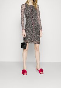 Mustapäinen ja vaaleanpunainen kuvioitu mekko, jossa on pitkät läpikuultavat hihat ja tiukka malli. Yhdistetty kirkkaan vaaleanpunaisiin korollisiin klompeihin, joissa on kukkakoristeita.