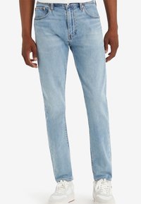 Jean en denim bleu clair à coupe droite, design à cinq poches avec un léger effet délavé ; porté avec des baskets blanches.