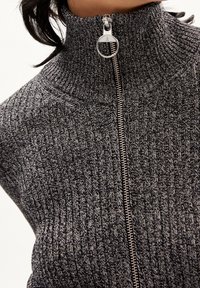 Suéter de punto negro y gris con cremallera, cuello alto, que presenta una cremallera plateada, un patrón de canalé texturizado y un ajuste ceñido.