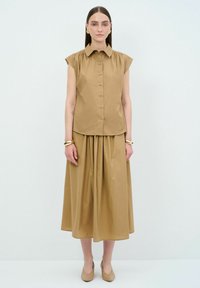 Brun skjorte med knap-ned front, korte ærmer og klassisk krave, parret med en matchende samlet nederdel, hvilket skaber et sammenhængende look.