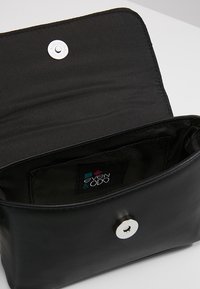 Borsa a mano in pelle nera con chiusura a scatto in argento, dotata di un interno texturizzato e un piccolo tag del brand con logo colorato all'interno.
