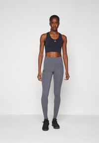 Sujetador deportivo negro y leggings grises de cintura alta hechos de material elástico, con un diseño ajustado y el logo de Under Armour en la pierna.