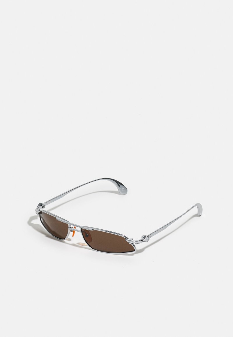 Lunettes de soleil avec une monture en métal argenté, des verres marron rectangulaires et des coussinets de nez orange. Branches fines avec une texture lisse et une légère courbure.